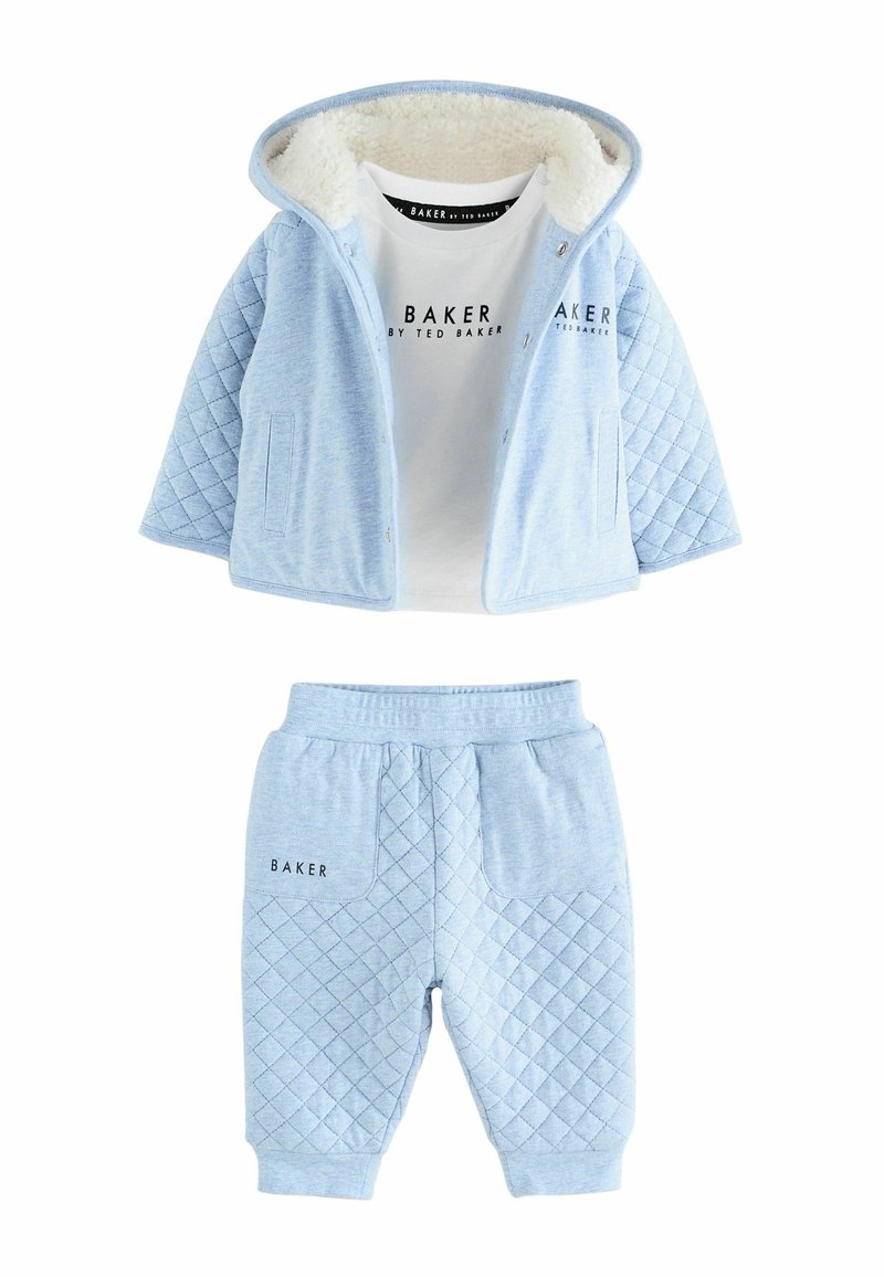 Giacca trapuntata blu chiaro con fodera in pelliccia bianca, abbinata a pantaloni joggers blu coordinati. Presenta una stampa del logo sulla maglia e sui pantaloni.
