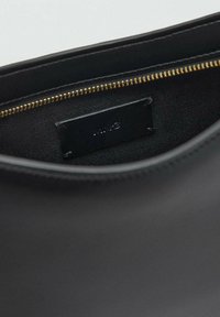 Black leather bag interior with a smooth texture, gold zipper, and a small leather tag. Minimalist design, no visible patterns or accents.
