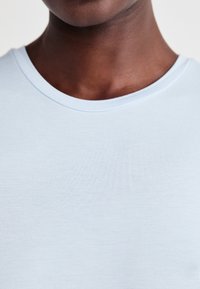 T-shirt azzurro chiaro con una superficie liscia, dotato di un colletto a girocollo e maniche corte, che mostra dettagli ravvicinati del tessuto e delle cuciture.
