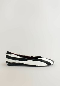 Chaussure plate présentant un motif zèbre noir et blanc, fabriquée en matériau souple avec un bout arrondi et un talon minimal. Texture lisse et silhouette simple.