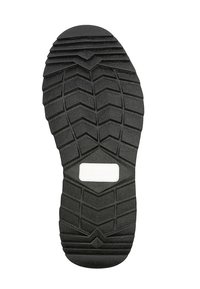 Suela de zapato de goma negra con patrones de relieve profundos y angulados, y una etiqueta blanca rectangular en el centro.