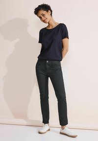 Pantalones negros ajustados con cierre de botón y bolsillos laterales, combinados con una camiseta azul marino texturada y zapatillas blancas con suela marrón.