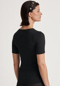 Top corto a maniche corte nero a costine con scollatura rotonda. Presenta un design aderente, una texture morbida e una silhouette pulita per un aspetto contemporaneo.