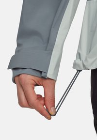 Waterdichte jas met een grijze buitenkant en lichtgrijze accenten; voorzien van verstelbare manchetten met elastische koordjes.