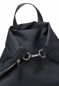 Sac à dos en nylon noir avec une ouverture arrondie, équipé de quincaillerie en acier argenté, d'une fermeture éclair et d'une courte poignée en tissu. Texture lisse.