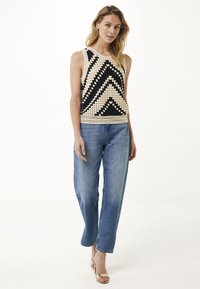 Virkningslinne i svart och kräm med ett zigzag-mönster, parat med ljusblå raka jeans och beigefärgade remsandaler.