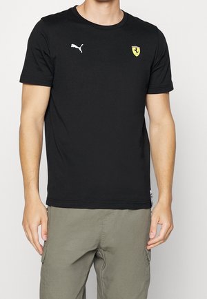 T-shirt en coton noir avec un col rond, arborant un logo Puma blanc sur le côté gauche de la poitrine et un logo de blason Ferrari jaune sur le côté droit.