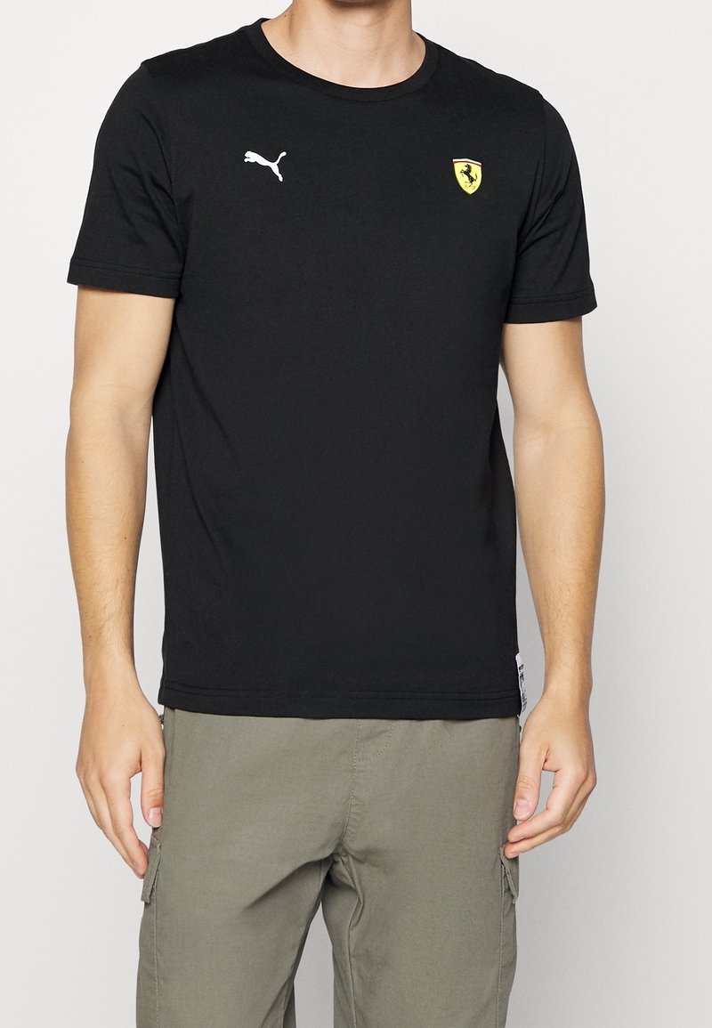 Černé bavlněné tričko s kulatým výstřihem, které má bílé logo Puma na levé straně hrudi a žluté logo štítu Ferrari na pravé straně.