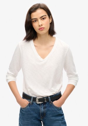 Witte langemouwen v-hals shirt, gemaakt van een lichtgewicht stof, gecombineerd met donkerblauwe denim jeans en een zwarte riem met een zilveren decoratieve gesp.