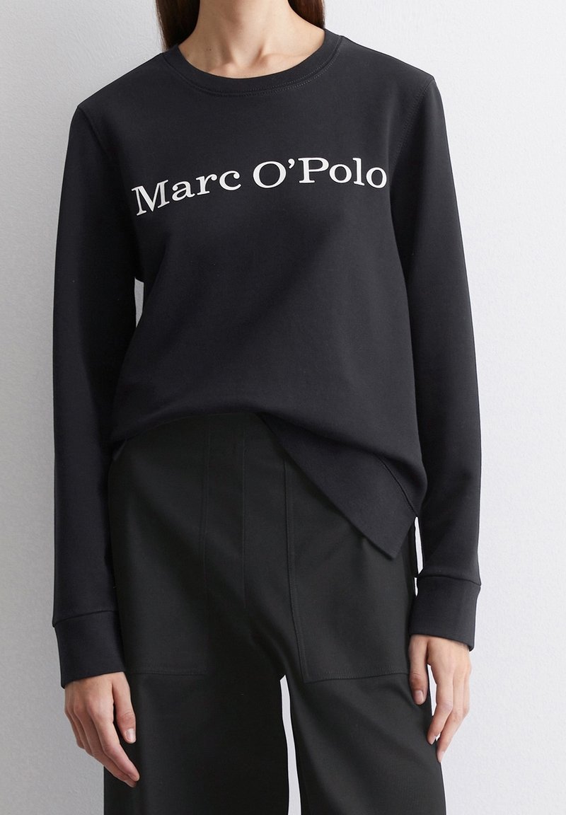 Czarny sweatshirt z białym napisem "Marc O’Polo", okrągły dekolt, długie rękawy i luźny krój, w połączeniu z czarnymi spodniami.
