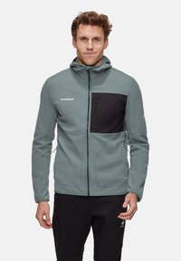 Mammut Fleecejacke in gedämpftem Blaugrün mit einer schwarzen Brusttasche, Kapuze und Reißverschluss, ausgestattet mit einer strukturierten Oberfläche für Wärme.