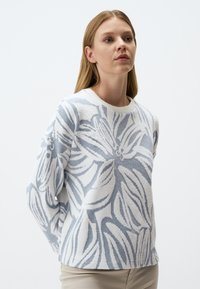 Maglione con motivo floreale in bianco e blu chiaro. Tessitura morbida, scollatura rotonda, vestibilità rilassata e maniche lunghe con delicati dettagli a foglia.