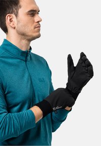 Schwarze Handschuhe mit gerippten Bündchen, ausgestattet mit einer strukturierten Grifffläche und elastischen Bändern. Getragen von einem Mann in einem türkisfarbigen Zip-Up-Shirt, der sich auf die Handschuhe konzentriert.