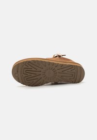 Braunes Schuhwerk mit strukturiertem Oberflächenmaterial und einer robusten Gummisohle, die ein geometrisches Muster aufweist. Enthält eine Schnürung zur Befestigung.