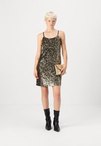 Vestido preto e dourado com lantejoulas, de alças finas, com um corte relaxado, que chega até à meia coxa. Combinado com uma mala dourada e botas pretas até ao joelho.