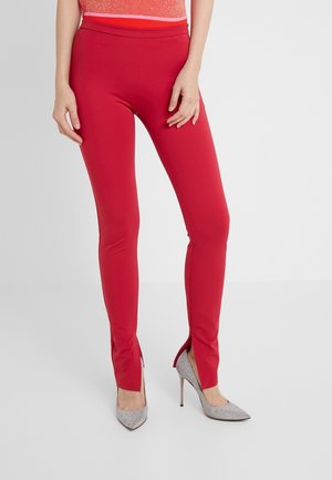 Czerwone elastyczne legginsy z rozcięciami po bokach u dołu, w zestawie z srebrnymi błyszczącymi szpilkami. Gładka tekstura, dopasowany krój.