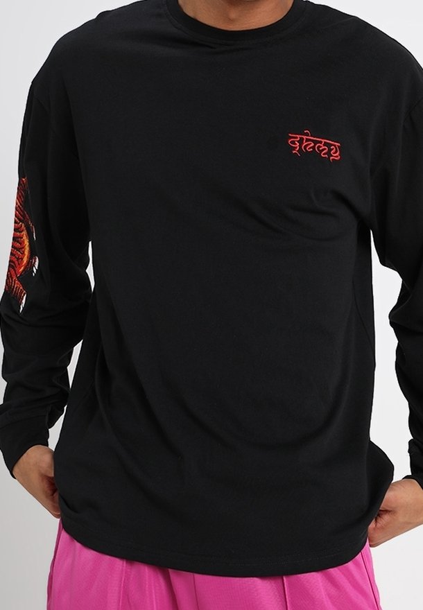 Mustapaita, jossa on pitkät hihat, valmistettu puuvillasta. Vasemmassa hihassa on punainen kuvio ja rintakehässä brodeeraus. Sujuva pinta.