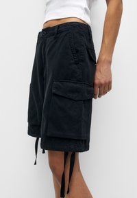 Pantalones cortos de carga negros de algodón, con un ajuste relajado, bolsillos laterales y cordones ajustables en el dobladillo.