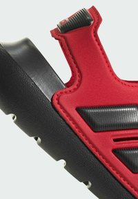 Bottines de sport rouges et noires avec une tige lisse dotée de découpes, des accents texturés et une semelle noire épaisse avec une adhérence à motifs.