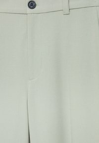 Pantalons ajustés vert clair avec une texture lisse, présentant un bouton noir et une couture soignée le long de la zone des poches.
