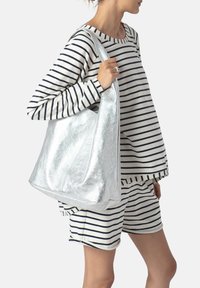 Metallisk silverfärgad hobo-väska med en shiny, slät yta och bred axelrem, kombinerad med en randig långärmad topp och shorts.