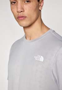 Ανοιχτό γκρι μπλουζάκι από απαλό ύφασμα με διακριτικό γεωμετρικό μοτίβο. Διαθέτει μικρό λε υκό λογότυπο στην αριστερή πλευρά του στήθους.