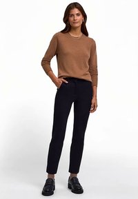 Brązowy sweter, czarne spodnie, oba dopasowane. Sweter ma długie rękawy i ściągacze; buty to czarne mokasyny o gładkiej fakturze.