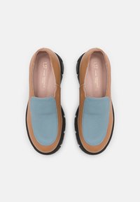 Chaussures en cuir à enfiler avec un corps marron, des accents texturés bleus et une semelle en caoutchouc noire. Fini l'intérieur lisse.