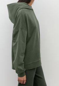 Sudadera con capucha de algodón verde con bolsillo canguro, puños acanalados y capucha con cordón. Textura suave y ajuste relajado. Detalle de costuras horizontales en los hombros.