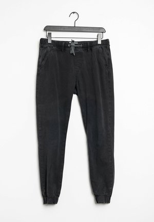 Pantalon jogger décontracté noir avec poignets élastiques et taille à cordon suspendu à un cintre noir sur fond blanc.