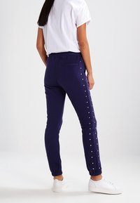 Navy joggers with side snap buttons, elastic waistband, and cuffs. Paired with a white short-sleeve t-shirt and white sneakers.