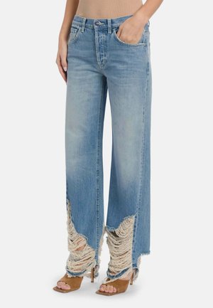 Jeans azzurri chiari a gamba larga con dettagli pesantemente sfrangiati e strappati sul fondo, indossati con sandali marroni con tacco e punta aperta.