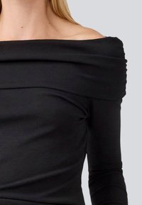 Top nero off-shoulder con scollatura drappeggiata, maniche lunghe, tessuto morbido e design aderente, che mette in mostra una superficie liscia e una finitura senza cuciture.