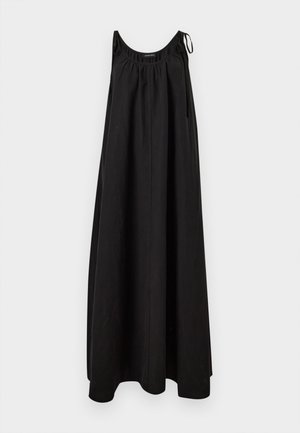 Femme portant une robe maxi noire sans manches, tenant une pochette jaune pâle et portant des sandales plates noires avec des accents dorés.
