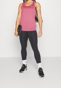 Fuchsia linne med racerback-design, svarta leggings och svarta träningsskor. Tillbehör inkluderar en viktskiva som hålls i ena handen.