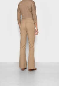 Pantalon beige évasé avec une texture lisse et des poches arrière, associé à un top marron ajusté et des chaussures marron, vu de dos.