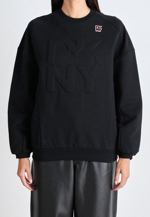 Svart sweatshirt i mjukt tyg med en upphöjd "DKNY"-logotyp. Ribbad avslutning på ärmar och nederkant samt ett litet märkespatch på bröstet.