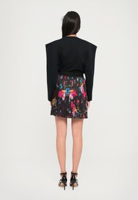 Top negro con hombreras combinado con una falda plisada de patrón floral con colores vibrantes y una cinturilla elástica negra, sobre un fondo liso.