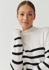 Pull blanc avec des rayures noires, col et poignets côtelés. Texture douce avec une coupe décontractée. Aucun motif ou détail matériel notable.