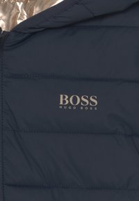 Navy puffer jacket with a shiny silver inner lining, featuring quilted panels. Embroidered "BOSS" logo in light grey on the front.
