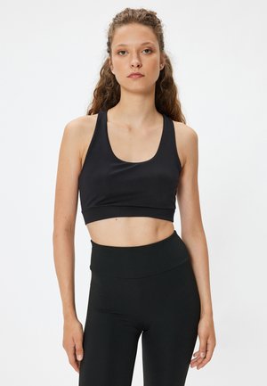 Sort sports crop top med scoop-halsudskæring og brede stropper, lavet af glat, strækbart materiale; parret med højtaljede sorte leggings.