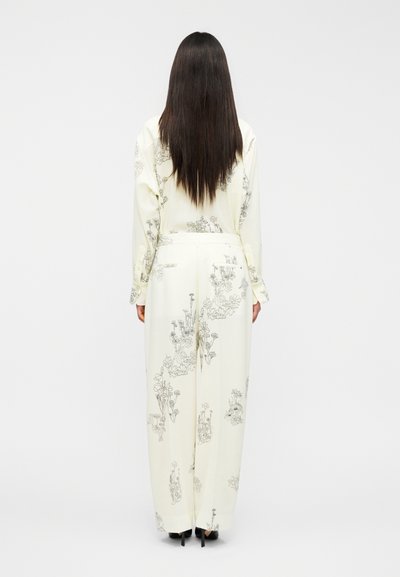 Μπλούζα εκρού με μακριά μανίκια και παντελόνι με φαρδιά μπατζάκια, διακοσμημένα με μαύρα λουλουδάτα σχέδια σε γραμμή, με πίσω τσέπες και μανσέτες με κουμπιά.