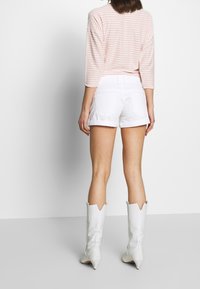 Top de rayas en rosa claro de manga larga combinado con pantalones cortos de mezclilla blancos. La modelo lleva botas vaqueras blancas de tacón con punta afilada.