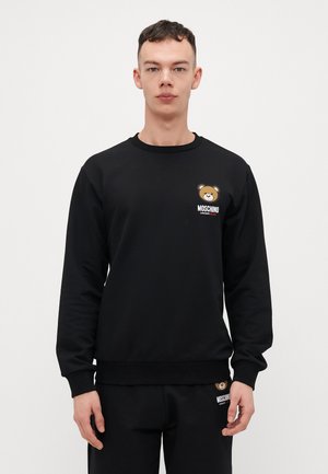 Musternudist mustrigu vest, valmistatud pehmest kangast, featuring karu graafika ja logo kontrastsetes värvides rinnal ja ääres.