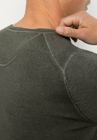 Dunkelgrünes T-Shirt mit kurzen Ärmeln aus strukturiertem, geripptem Stoff und rundem Halsauschnitt, mit ausgeprägten Schulternähten und minimalen Nähten.