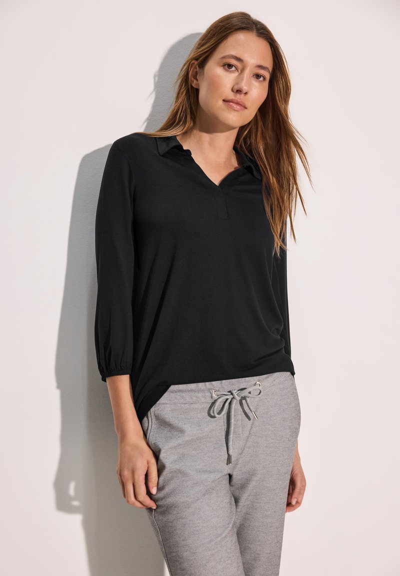 Schwarzes Langarmoberteil mit kragenförmigem Ausschnitt und lockerer Passform, kombiniert mit hellgrauen Sweatpants mit Kordelzugbund.