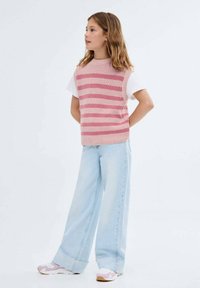 Růžovo-bíle pruhovaná pletená vesta přes bílé tričko, doplněná světle modrými kalhotami s širokými nohavicemi a teniskami s růžovými akcenty.