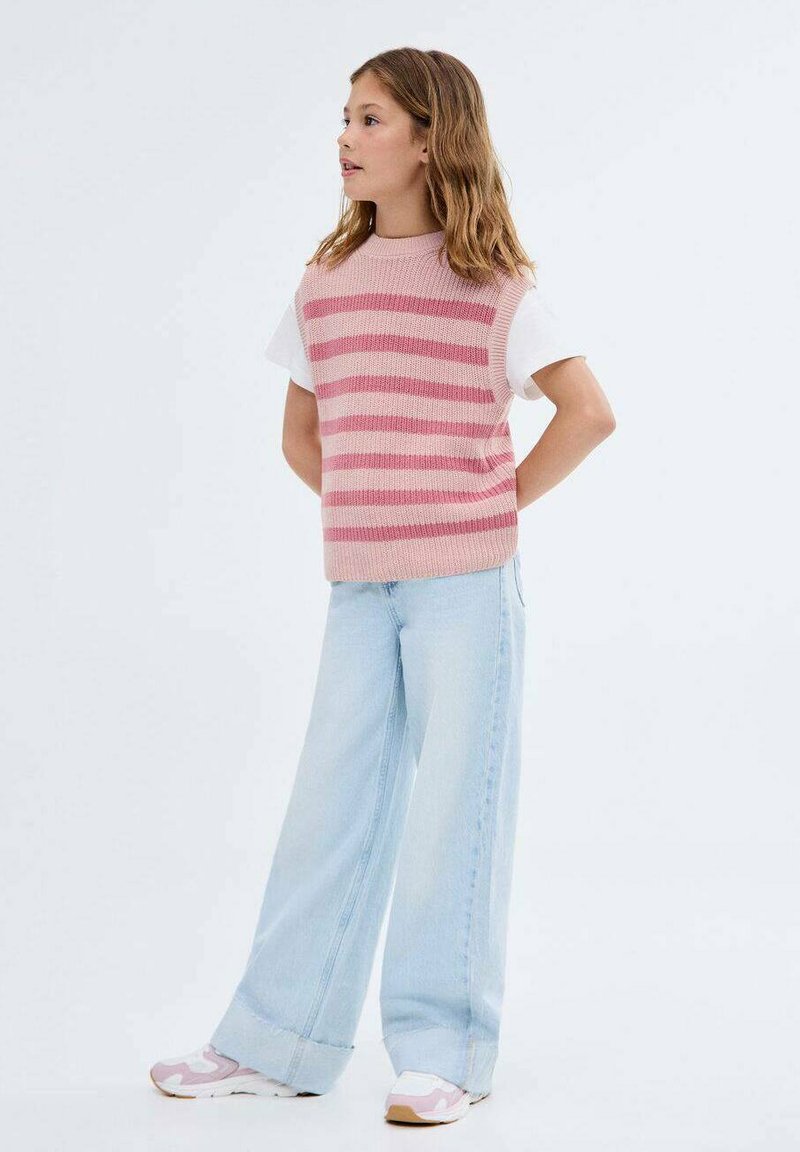 Růžovo-bíle pruhovaná pletená vesta přes bílé tričko, doplněná světle modrými kalhotami s širokými nohavicemi a teniskami s růžovými akcenty.