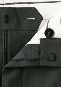 Zbliżenie na pas ciemnozielonych spodni z guzikiem, zamkiem błyskawicznym, zapięciem na hak i oczko oraz białą podszewką z czarną lamówką.