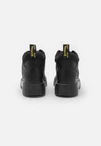 Svarta ankelstövlar i texturerat läder, kraftiga gummisulor och gula accenttaggar som säger "MED BOUNCING SOLES" vid hälen.